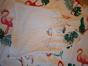 Vit linnetopp med spets och broderi - Säljer en vit linnetopp från Gina Tricot med smala axelband och v-ringad hals. Toppen har fina spetsdetaljer och broderade blommor framtill samt ett dekorativt tryck. Perfekt för sommarens alla dagar!