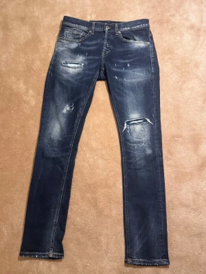 Mörkblå skinny jeans från George - Säljer ett par mörkblå skinny jeans från George med slitningar och trasiga detaljer på benen. Jeansen har klassisk femficksdesign, orange sömmar och skinny fit som sitter tajt längs benen. Perfekt för dig som gillar en edgy och modern look. Skick 9.5-10. Nypris 4000kr Mitt 649kr Storlek 32