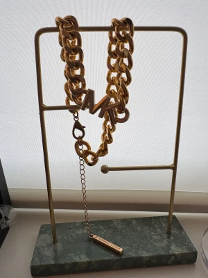 Guldigt halsband Michael Kors - Chunky halsband i guldtonad metall från Michael Kors med grova länkar och MK-logga framtill. Justerbar längd med kedja och bricka där märket är ingraverat. Perfekt statement piece för dig som gillar att sticka ut.