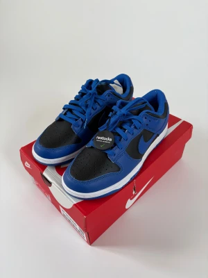 Nike Dunk Low Retro Hyper Cobalt - Nike Dunk Low Retro i färgen Hyper Cobalt och svart. Klassisk low-top siluett med blå och svarta paneler i skinn, vit mellansula och blå yttersula. Snygga snörade sneakers med retrovibbar och tydlig Nike-logga på hälen. Perfekta för dig som gillar streetstyle. Kom gärna med pris förlag. Ny pris 3000