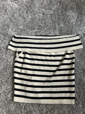 Randig offshoulder tröja från H&M, stl S - Snygg kortkjol från H&M i storlek S med klassiska svarta och vita ränder. Kjolen är ribbstickad och har en bred, vikt linning som ger en cool och modern look. Perfekt för dig som gillar en enkel men trendig stil.