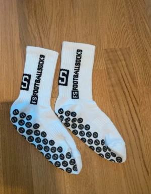 FS Footballsocks vita träningsstrumpor - Säljer ett par vita FS Footballsocks med svart logga och text längs skaftet. Strumporna har svarta gummigrepp under foten för extra fäste vid träning eller fotboll. Ribbad design vid skaftet och tillverkade i mjuk och slitstark bomullsmix.Passar personer med storlek 35 