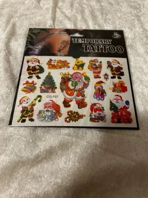 Juliga temporära tatueringar - Ett ark med färgglada temporära tatueringar med julmotiv, bland annat tomtar, julgranar, presenter och godis. Perfekt för att piffa upp din look under december! Motiven är detaljerade och kommer i olika former och storlekar. Appliceras enkelt med vatten.