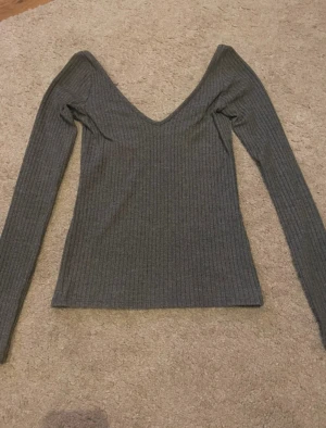 Grå ribbad långärmad topp H&M - Säljer en grå ribbad långärmad topp från H&M i storlek 32. Toppen har en djup v-ringning och är figurnära i modellen. Perfekt att styla med jeans eller kjol för en chill och snygg look.