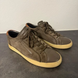 Bruna sneakers från Dolce & Gabbana - Snygga sneakers från Dolce & Gabbana i brun mocka och skinn med beige sula. Skorna har snörning, rund tå och en quiltad innersula för extra komfort. Bakpartiet har en detalj i ljusbrunt skinn som ger en cool kontrast. Perfekta för dig som gillar stilrena och exklusiva sneakers. Storlek 42