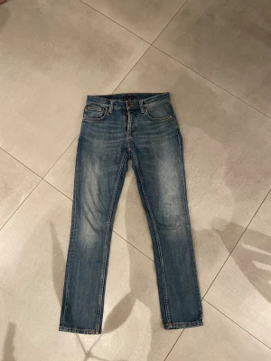 Nudie jeans blå - Tja säljer nu ett par feta ljusblå jeans från Nudie  med slim passform och klassisk femficksdesign. Jeansen har blå sömmar, knappar framtill.  Perfekt för dig som gillar en clean och stilren look. Skicket är helt perfekt som nytt ungefär och storleken w28 l30 är passar dig som är runt 167-175 lång skulle jag tro!! Har du några övriga frågor är de bara att höra av sig🙌🏼mvh em_resell🤩