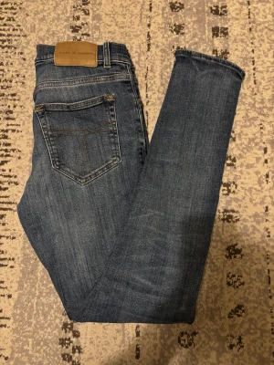 Tiger of Sweden blå jeans Evolve 29/32 - Snygga blå jeans från Tiger of Sweden, modell Evolve, tillverkade i Italien. Klassisk femficksdesign med kontrastsömmar och läderpatch bak i midjan. Jeansen har rak passform och är gjorda i slitstarkt denimtyg.