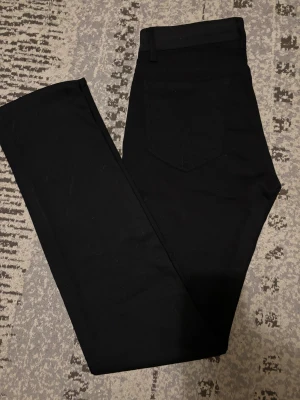 Svarta straight jeans Tiger of Sweden - Svarta jeans från Tiger of Sweden i straight modell. Klassisk femficksdesign med snyggt svart läderpatch bak i midjan. Jeansen är tillverkade i ett mjukt och slitstarkt material som sitter skönt och har en stilren look.