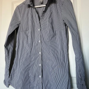 Svart/vit randig H&M skjorta - Bekväm, figurnära och fin svart/vit randig skjorta från H&M. I väldigt bra skick. Storlek 40, normal i storleken. Passar även 36/38, men en lösare passform. Original extra knapparna kommer med (bild 3).