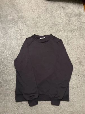 Svart sweatshirt från D.M.D  - En stilren svart sweatshirt från D.M.D med rund hals och diskret X-detalj vid halsringningen. Tröjan har långa ärmar och ribbade muddar vid ärmslut och nederkant. Perfekt för dig som gillar enkel och clean stil. Passar perfekt i skolan eller hemma. För dig som vill ha lite extra stil i vardagen. 