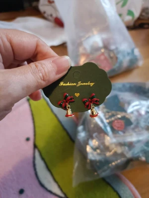 Juliga örhängen med rosett och klocka - Snygga örhängen med röda och gröna rosetter samt små guldfärgade klockor som hänger ned. Perfekta för att maxa julstämningen och ge din look en festlig touch. Säljs på originalkortet från Fashion Jewelry.
