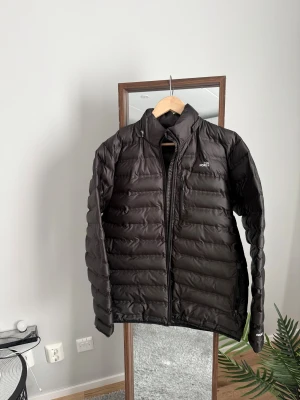 Svart dunjacka från The North Face - Säljer en svart dunjacka från The North Face med klassisk puffer-design. Det enda är en liten defekt framtill vid märkestrycket: två bokstäver har lossnat lite från tyget. Det påverkar inte användningen. Storlek L 