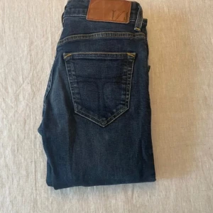 Mörkblå jeans från Levis - Snygga mörkblå jeans från Levis med klassisk femficksdesign och brunt läderpatch bak i midjan. Jeansen har raka ben och kontrastsömmar, perfekta för en stilren look. Passar dig som gillar tidlös denim.