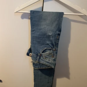 Blå jeans med klassisk passform - Säljer ett par blå jeans med klassisk femficksdesign och knappgylf. Jeansen har en ljus tvätt och synliga sömmar, perfekta för en avslappnad stil. Passar dig som gillar en enkel och tidlös look.