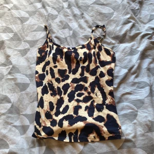 Leopardmönstrad linnetopp i beige och svart - Säljer en snygg leopardmönstrad linnetopp i beige, svart och bruna toner. Toppen har smala axelband och är tillverkad i ett stretchigt material som sitter skönt på kroppen. Perfekt att styla med jeans eller kjol för en cool look.
