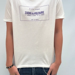 Vit t-shirt från Zadig & Voltaire - Vit t-shirt med lila tryck framtill från Zadig & Voltaire. Klassisk passform med rund hals och korta ärmar. Tillverkad i mjuk bomull, perfekt för en avslappnad och stilren look.