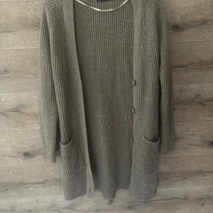 Brun ribbad kofta från Gina Tricot - Mysig lång kofta i brun nyans från Gina Tricot. Koftan är ribbstickad, har knappar framtill och två stora fickor. Perfekt att slänga på sig över en t-shirt eller topp när det är kyligt ute.