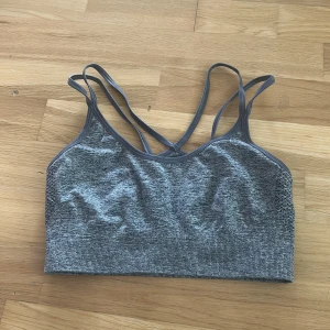 Grå sporttopp från Röhnisch - Säljer en grå sporttopp från Röhnisch med smala korsade axelband och melerat mönster. Toppen är tillverkad i ett stretchigt material med polyamid och elastan, perfekt för träning. Snygg och enkel design som sitter skönt på kroppen.