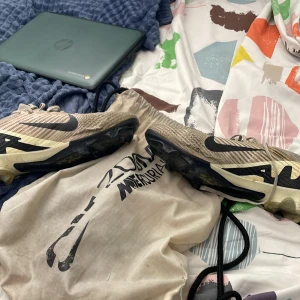 Nike Air Zoom Mercurial fotbollsskor - Säljer ett par Nike Air Zoom Mercurial fotbollsskor elite i beige och svart med coolt grafiskt mönster på sidan. Skorna har snörning, platt sula med dobbar och är tillverkade i syntetmaterial med stickad ovandel för grym passform. Perfekta för dig som vill ha speed och kontroll på planen.