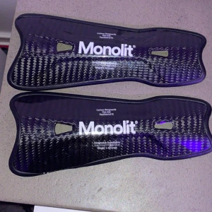 Monolit benskydd i kolfiber - Säljer ett par svarta Monolit benskydd bra skick och världens lättaste benskydd i kolfiber med snyggt mönster och vit logga. Lätta och smidiga med ergonomisk form, designade i Skandinavien. Perfekta för dig som vill ha maxad skyddsnivå och stil på planen.  