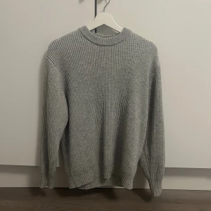 Grå ribbstickad tröja från Zara - Säljer en grå ribbstickad tröja från Zara i storlek M. Tröjan har rund halsringning och långa ärmar, perfekt för lager-på-lager. Den är stickad i ett mjukt material och har en klassisk, enkel look som funkar till allt.