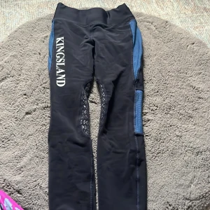 Svarta ridleggings från Kingsland - Snygga svarta ridleggings från Kingsland med blå detaljer längs sidorna och silikongrepp på insidan av benen. Modellen har hög midja och elastiskt material som ger bra passform och rörelsefrihet. Perfekta för dig som gillar ridning och vill ha stil på stallet.  Storleken står inte men funkar för nästan alla. själv har jag 158 i storlek och xs men är lite stor för mig men syns knappt💕 använt en gång