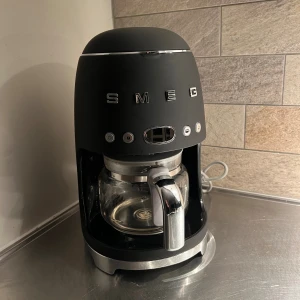 Smeg Kaffebryggare DCF02 - Stilren Smeg kaffebryggare i svart med retrodesign. Glasbehållare, digital display och flera brygginställningar.  mycket gott skick . Perfekt för dig som vill ha både design och funktion i köket.