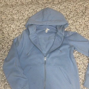 Ljusblå hoodie med dragkedja från H&M - Säljer en ljusblå hoodie från H&M i storlek XS. Tröjan har dragkedja framtill, huva med snörning och två fickor. Perfekt för chill dagar och enkel att matcha med jeans eller mjukisbyxor.