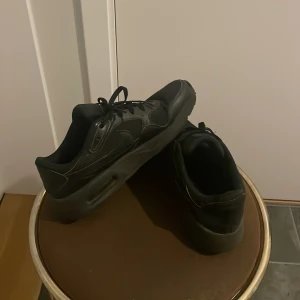 Svarta Nike sneakers med snörning - Säljer ett par helsvarta Nike sneakers med klassisk design och snörning. Skorna har en chunky sula och diskret Nike-logga på sidan. Perfekta för dig som gillar en clean och stilren look. Passar till det mesta och är riktigt bekväma.