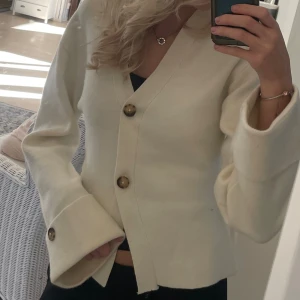 Kofta från Gina - Superfin krämvit kofta från Gina Tricot med v-ringning och stora bruna knappar framtill och på ärmsluten. Typ helt oanvänd så i super from skick.