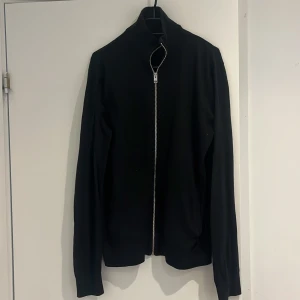 Svart kofta från Jack & Jones - Svart kofta från Jack & Jones med hel dragkedja framtill och hög krage. Tröjan är långärmad och har en clean, stilren look som passar perfekt till lager-på-lager. Materialet är mjukt och känns skönt mot huden.