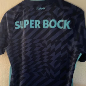 FC Porto bortatröja New Balance blå - Snygg FC Porto bortatröja från New Balance i mörkblått med ljusblå detaljer och geometriskt mönster. Tryck med klubbmärke, sponsorloggor och V-ringad krage. 