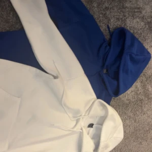 Vita och blå hoodies från SHEIN XS - Två stilrena hoodies från SHEIN i storlek XS, en i klassiskt vitt och en i djupblå färg. Båda har huva, långa ärmar och känguruficka framtill. Perfekta för en chill och avslappnad look. Materialet är mjukt och känns skönt mot huden.