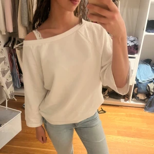 Vit offshoulder tröja med vida ärmar - Vit tröja från Nelly med offshoulder-design och vida, trekvartsärmar. Tröjan har en avslappnad passform och är gjord i mjukt bomullsmaterial. Perfekt för dig som gillar en chill och stilren look. 