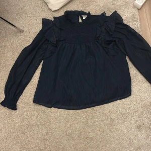 Mörkblå volangblus med smock - Pris går att diskutera och skicka ifall ni vill att jag ska prova den Supersöt mörkblå blus från Gina Tricot med volangdetaljer på axlarna och smockad överdel. Blusen har långärmade, lätt transparenta ärmar och hög krage med rynk. Materialet är tunt och glansigt, vilket ger en lyxig känsla. Perfekt för dig som gillar romantisk 🥰 stil.