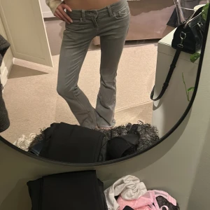 Grå bootcut jeans med broderade fickor - Säljer ett par gråa jeans med bootcut-modell och snygga broderade detaljer på bakfickorna. Jeansen har låg midja och klassisk femficksdesign. Materialet är jeans och passformen är normal. Perfekta för dig som gillar en stilren men ändå unik look.