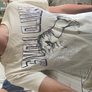 Beige  t-shirt med enhörning 🦄  - Cool beige  t-shirt från Lindex med stort tryck av en häst och texten 'WILD LOVE' i lila och svart. T-shirten har korta ärmar och är gjord i mjuk bomull. Perfekt för dig som gillar hästar och vill sticka ut med en unik design.