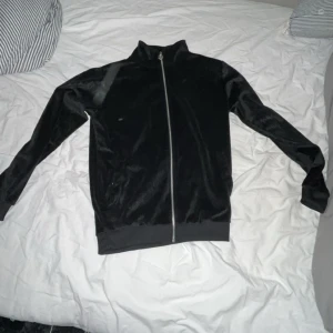 Svart sammetströja från Black Squad XS - Svart långärmad tröja från Black Squad i mjuk sammet med hel dragkedja framtill. Tröjan har hög krage och ribbade muddar vid ärmslut och nederkant. Perfekt för dig som gillar en clean och stilren look.