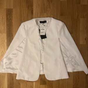 Vit kavaj från Zara Woman, stl M - Snygg vit kavaj från Zara Woman i storlek M. Kavajen har en stilren, rak passform utan knappar, med två fickor framtill och helfodrad insida. Tillverkad i ett slätt tyg som ger en clean look. Perfekt för dig som vill ha en fräsch och modern stil.