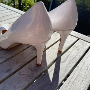 Vita lackpumps från Tiamo - Snygga vita pumps från Tiamo i glansigt lackmaterial. Skorna har spetsig tå och hög klack