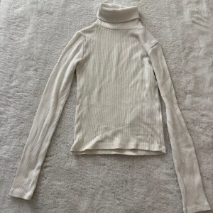 Vit ribbad polotröja med långa ärmar - Säljer en stilren vit polotröja med ribbad struktur och långa ärmar. Perfekt för lager-på-lager och passar till allt. Hög krage som ger en snygg siluett och extra värme. Enkel att matcha med både jeans och kjol.