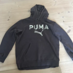 Svart hoodie från Puma med logga - Svart hoodie från Puma med stor vit logga och text på bröstet. Klassisk känguruficka framtill, huva med snörning och långa ärmar. Perfekt för en chill och sportig stil. Den är lite smutsig men bara en tvätt gör att de försvinner:)