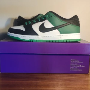 Nike SB Dunk Low Pro Classic Green - Nike SB Dunk Low Pro i färgen Classic Green med svart, vitt och grönt skinn. Skorna har gröna snören, svart swoosh och vit mellansula med grön yttersula. Perfekta för dig som gillar streetwear och skate. Kommer med extra vita skosnören och originalkartong. Helt nya. Oanvända