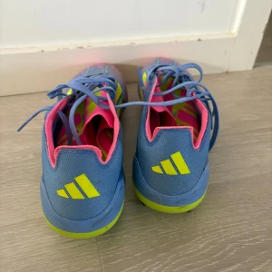 F50 blå/gul fotbollsskor - Säljer ett par Adidas f50  fotbollsskor i blått med neon-gula och rosa detaljer. Skorna har snörning, låg profil och är tillverkade i syntetmaterial. Perfekta för dig som vill sticka ut på planen med färgstark stil och grym passform.