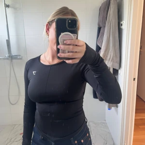 Svart långärmad topp med öppen rygg - Säljer en långärmad topp från Gymshark i stretchigt syntetmaterial som inte längre säljs. Toppen har en tight passform och en stor, rundad öppen rygg som formar ryggen på ett väldigt snyggt sätt💕säljer så den inte kommer till användning, endast använd någon gång