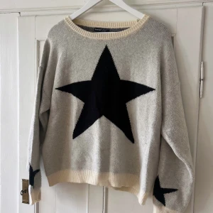 Beige stickad tröja med svarta stjärnor - Beige stickad tröja från SHEIN med stora svarta stjärnor på bröstet och ärmarna. Tröjan har rund halsringning, ribbade muddar och en loose passform. Perfekt för dig som gillar en chill och trendig stil.