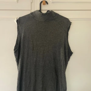 Trendig polotopp - Säljer en mörkgrå ärmlös polotopp med hög ribbad krage. Klippt bort ärmarna själv och därmed hackigt. Polokrage. Storlek L men passar mig perfekt som har storlek S i vanliga fall. 