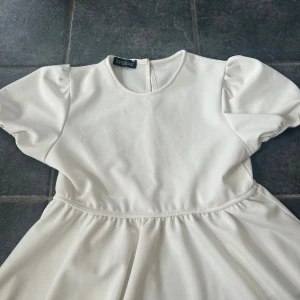 Vit blus med puffärm från Missay - Supersöt vit blus från Missay med puffiga korta ärmar och rund halsringning. Blusen har en lätt utställd kjol och slät yta, perfekt för dig som gillar en clean och stilren look.