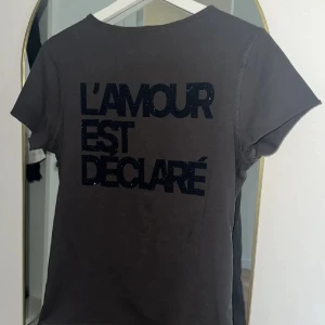 Svart t-shirt Zadig & Voltaire - Såå snygg Svart t-shirt från Zadig & Voltaire med texten 'L'AMOUR EST DÉCLARÉ' i glittriga bokstäver på ryggen. Kortärmad modell med lätt v-ringad hals och små knappar längs kanten🖤