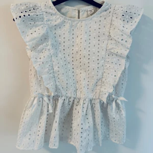 Vit volangblus från SHEIN - Supersöt vit klänning från SHEIN med broderade hålmönster, volanger längs axlarna och små knytband i midjan. 